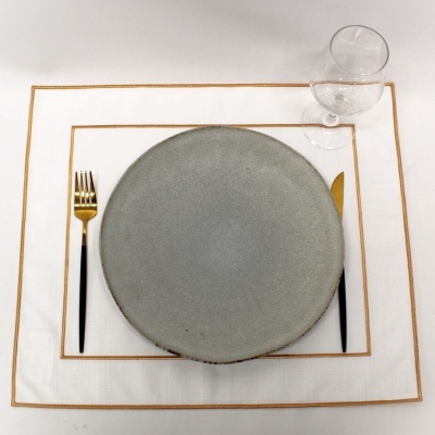 Conjunto de jantar com prato cinzento, talheres dourados e toalhinha branca com bordos dourados