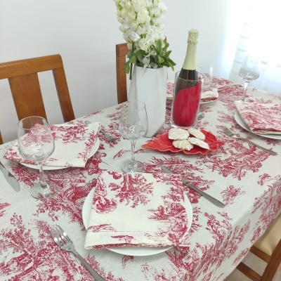Mesa posta com toalha vermelha e branca, pratos, copos, talheres e jarro com flores