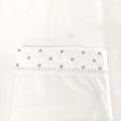 Fronha branca com bordado de círculos cinza na borda superior