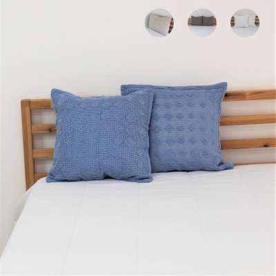 Almofadas azuis texturizadas numa cama com roupa de cama branca e estrutura de madeira.