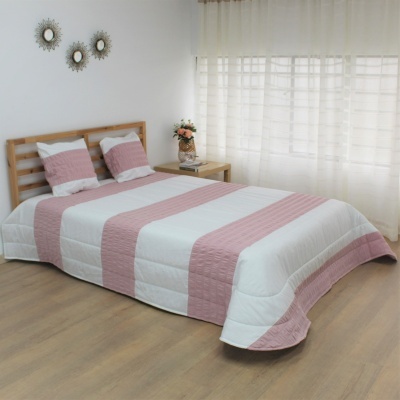 Cama com edredão branco e riscas cor de rosa num quarto com chão de madeira e cortinas brancas