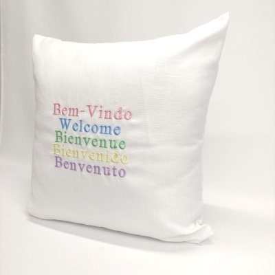Almofada branca bordada com mensagens de boas-vindas em várias línguas e cores