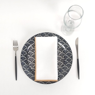 conjunto de jantar com prato azul padrão escamas, guardanapo branco, talheres pretos e taça de vidro