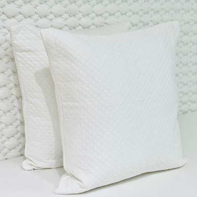 Duas almofadas quadradas brancas em superfície e parede brancas com texturas discretas.