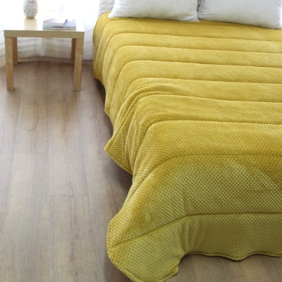 Colcha amarelo texturizada acolchoada em cama ao lado de mesa de madeira clara
