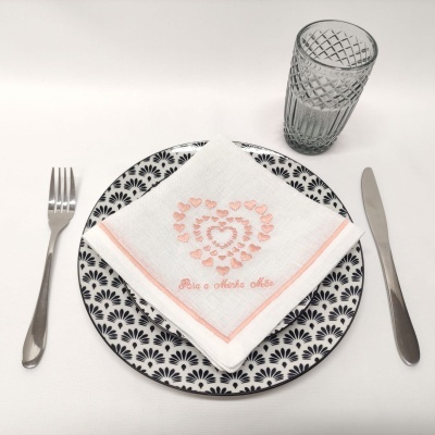 Conjunto de loiça com prato, guardanapo bordado, copo de vidro e talheres sobre mesa branca