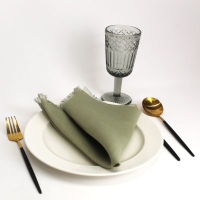 Conjunto de prato branco com guardanapo verde, copo cinzento e talheres pretos com dourado
