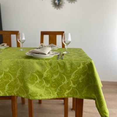 Toalha de mesa verde com padrão decorativo sobre mesa de madeira com pratos, guardanapos, talheres e copos, espelhos na parede ao fundo