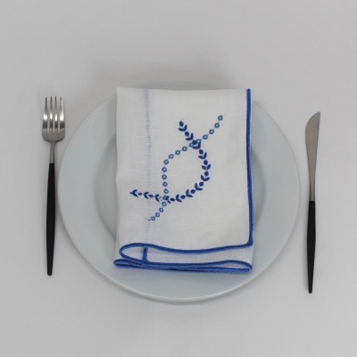 Talheres, prato branco e guardanapo branco bordado em azul sobre fundo cinzento