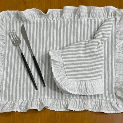 Jogo americano e guardanapo de tecido com riscas cinza e branco e bordas franzidas, com talheres de cabo preto sobre superfície de madeira.