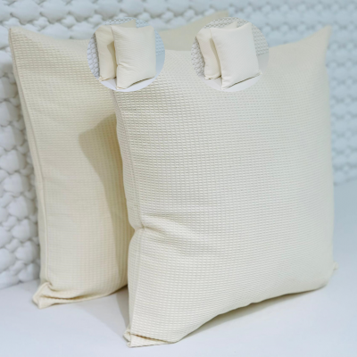 Duas almofadas creme com textura quadriculada sobre superfície branca e fundo acolchoado