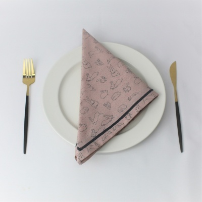 Guardanapo rosa com desenhos pretos sobre prato branco e talheres dourados