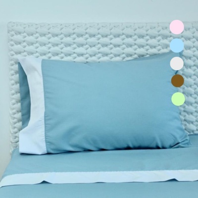 Almofada azul com borda branca em cama com cabeceira branca acolchoada