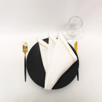 Conjunto de serviço de mesa com prato preto, guardanapo branco, talheres com dourado e copo de vidro