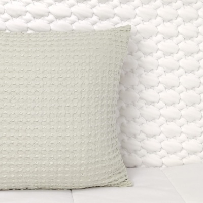 Almofada cinzenta clara com textura bolinhas sobre fundo branco trançado acolchoado