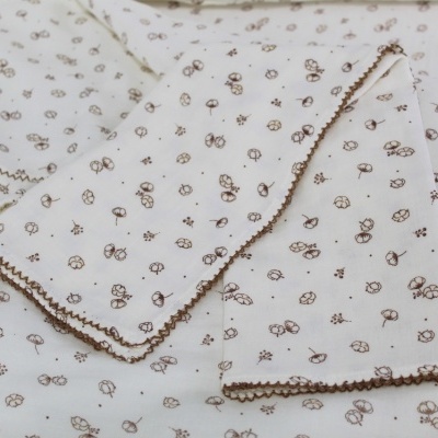 Tecido branco com padrão de pequenas flores e folhas castanhas e bordas decorativas castanhas