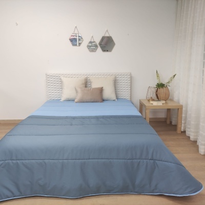 Cama com roupa de cama azul e almofadas, mesa de cabeceira com decoração, parede branca com espelhos hexagonais