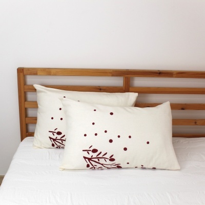 Almofadas creme com padrão vinho em cama com cabeceira de madeira clara