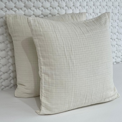 Duas almofadas brancas com textura quadriculada em fundo branco e parede decorativa