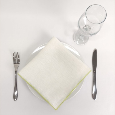 Mesa posta com prato branco, guardanapo branco com borda verde, talheres de metal e copo de vidro