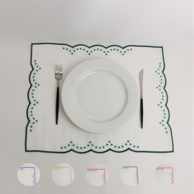 Guardanapo branco com borda verde e pontos, prato branco, talheres com cabo preto