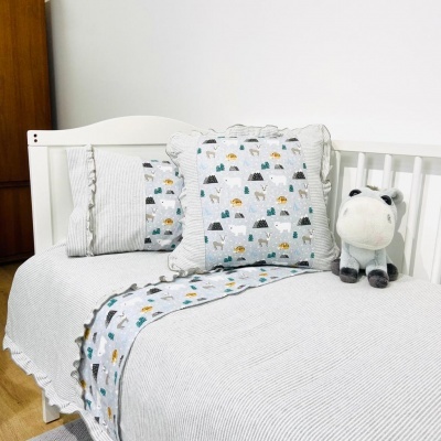 Cama de bebé branco com roupa de cama cinzenta e almofada com padrão de montanhas e animais