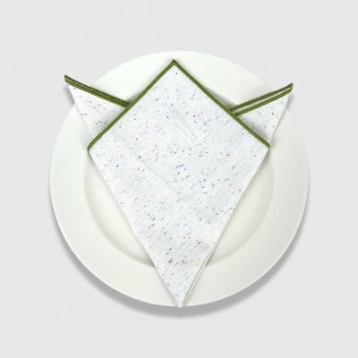 Guardanapo branco com pontos coloridos e bordas verdes em prato branco.
