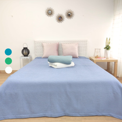 Cama com colcha azul clara, almofadas rosa, mantas enroladas, abajur e abajur numa decoração de quarto moderna