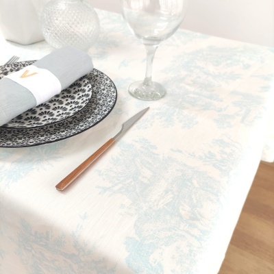 Mesa posta com toalha branca e azul, pratos pretos e brancos, guardanapo cinzento com argola, faca com cabo de madeira e copo de vidro