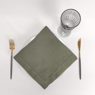 Conjunto de mesa com guardanapo verde, prato branco, talheres pretos e dourados e copo de vidro com padrão