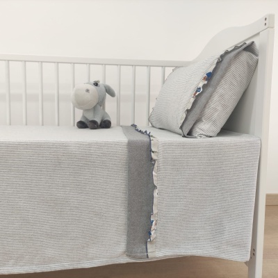 Cama de bebé branca com roupa de cama cinzenta e peluche de burro