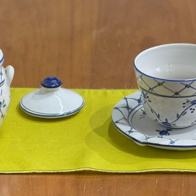 Conjunto cerâmico branco e azul com chávena, pires e açucareiro sobre pano amarelo