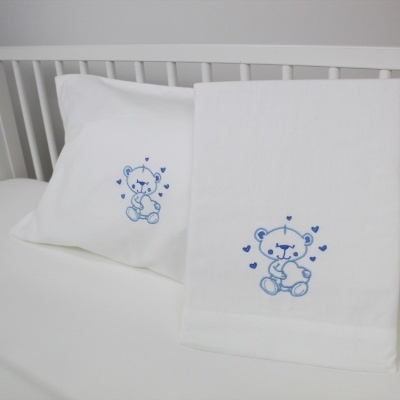 Conjunto de fronha e toalha branca com bordado de ursinho azul em cama branca