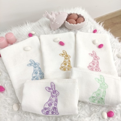 Toalhas brancas com coelhos coloridos estampados sobre superfície felpuda com ovos decorativos e recipiente em forma de ovo