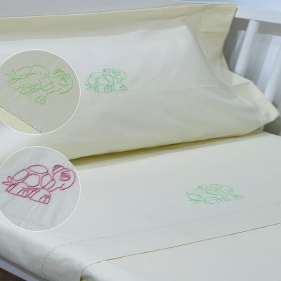 Jogo de cama branco com bordados de tartarugas verdes e rosas numa cama de grades branca