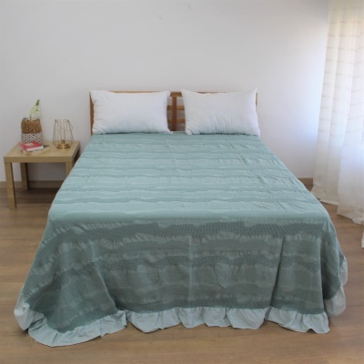 Cama com colcha verde-água texturada e almofadas brancas numa decoração minimalista.