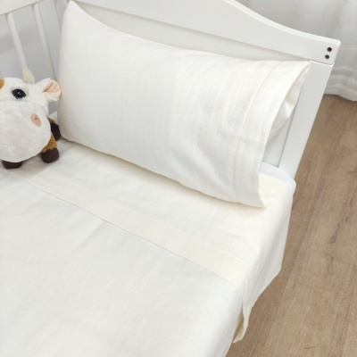 Cama de berço com roupa de cama branca e peluche de vaca ao lado