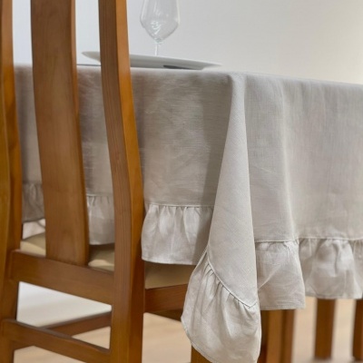 Toalha de mesa bege com bainha franzida sobre mesa de madeira