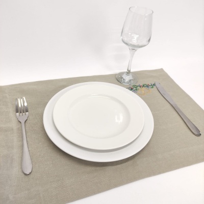 Serviço de mesa com pratos brancos, talheres metálicos, copo de vidro e individual bege com bordado colorido