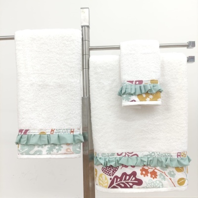 Toalhas de banho brancas com bordados florais coloridos e folhos verdes penduradas