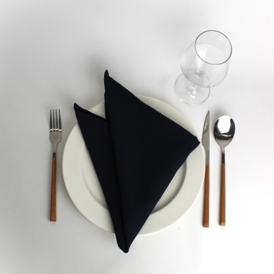 Conjunto de mesa com prato branco, guardanapo preto, talheres de cabo castanho e taça de vidro