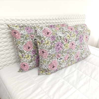 Duas fronhas florais coloridas sobre cama branca com cabeceira texturizada