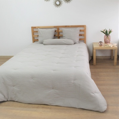 Cama de casal com roupa de cama cinzenta com pontos brancos e cabeceira em madeira clara