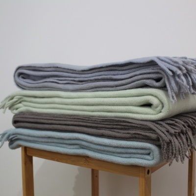 Quatro mantas coloridas empilhadas sobre banco de madeira.