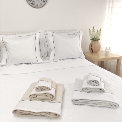 Roupas de cama e toalhas dobradas em cama branca com decoração minimalista.