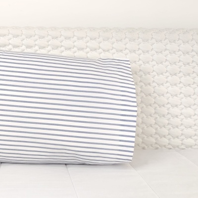 Travesseiro branco com riscas azuis numa cama com cabeceira branca acolchoada