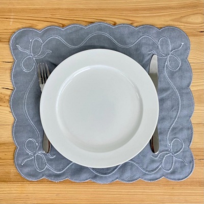 Lugar americano cinzento com bordado e talheres sobre mesa de madeira