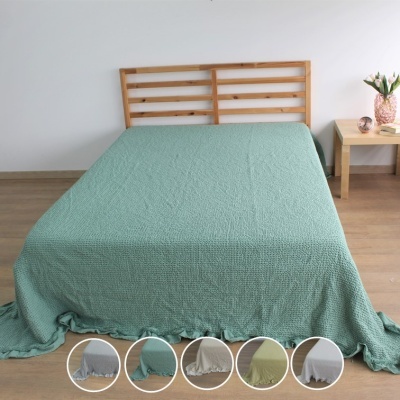 Colcha verde água texturizada com babados numa cama com cabeceira de madeira clara e mesa de cabeceira com vaso e objetos decorativos
