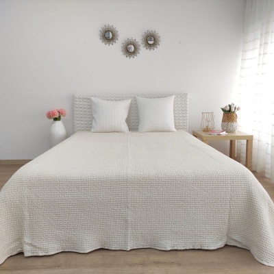 Cama com colcha branca texturizada e decorações minimalistas