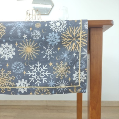 Toalha de mesa decorativa com flocos de neve em cinza, branco e dourado sobre mesa de madeira